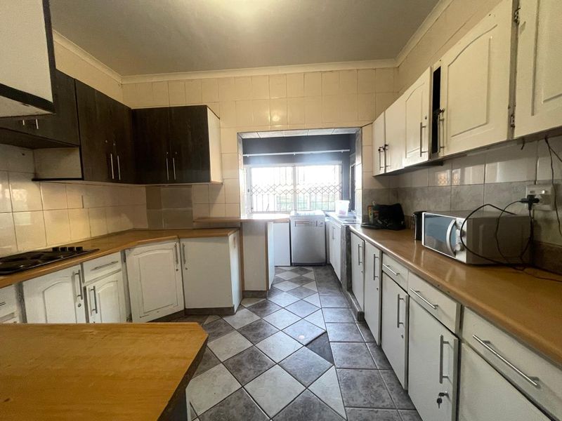 A dated kitchen featuring two-tone cabinetry, laminate countertops, and ceramic tile flooring, offering significant potential for a modern renovation.