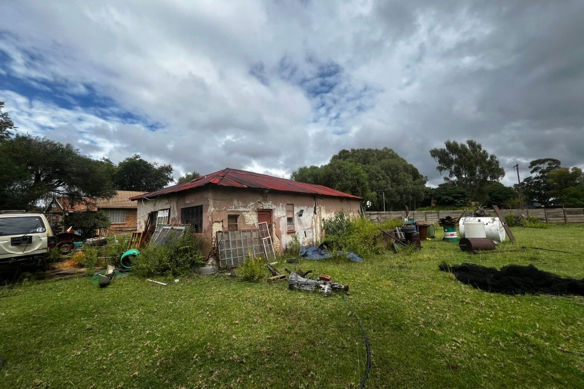 Rear view of a property showing a detached structure with a corrugated metal roof and significant exterior wall deterioration, set on a large plot.