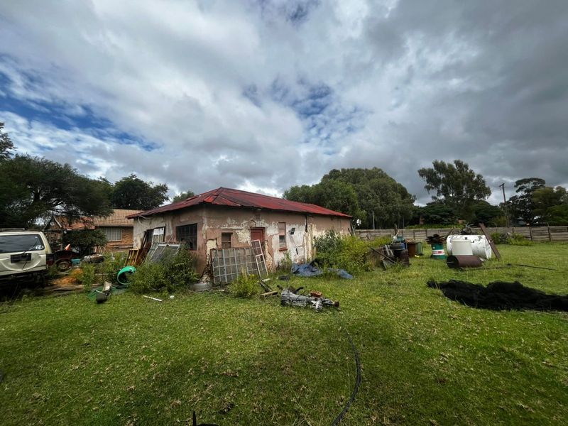 Rear view of a property showing a detached structure with a corrugated metal roof and significant exterior wall deterioration, set on a large plot.