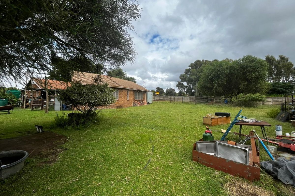 A view of the rear exterior of the brick house, featuring a large garden area and perimeter fencing.