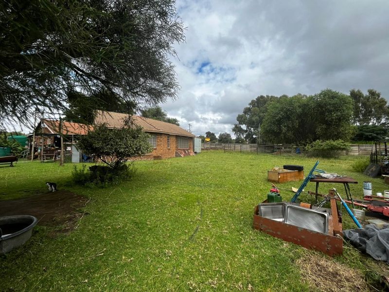 A view of the rear exterior of the brick house, featuring a large garden area and perimeter fencing.