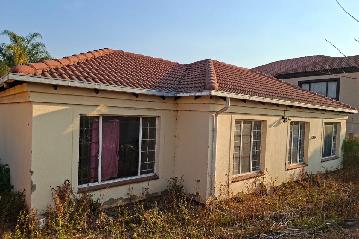 Rear exterior view of a single-story house featuring a tiled roof, security bars on windows, and exterior walls requiring maintenance and landscaping.