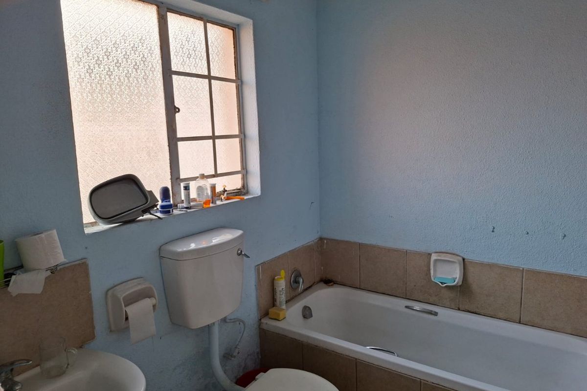 A dated bathroom featuring a standard bathtub, toilet, and pedestal basin with tiled splashbacks and an obscured glass window.