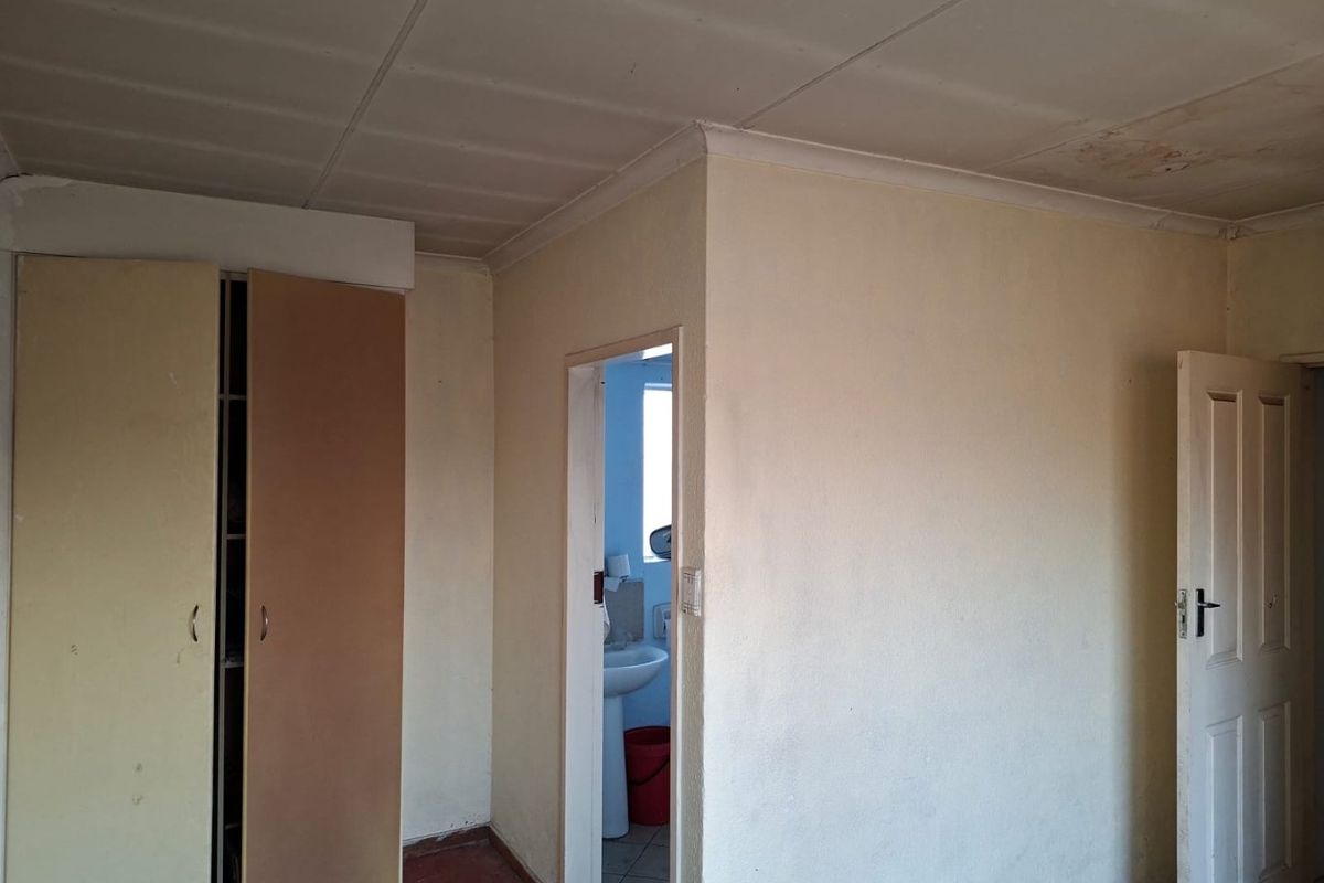 An empty bedroom featuring a built-in wardrobe and access to an adjoining bathroom, requiring cosmetic updates and ceiling repairs.