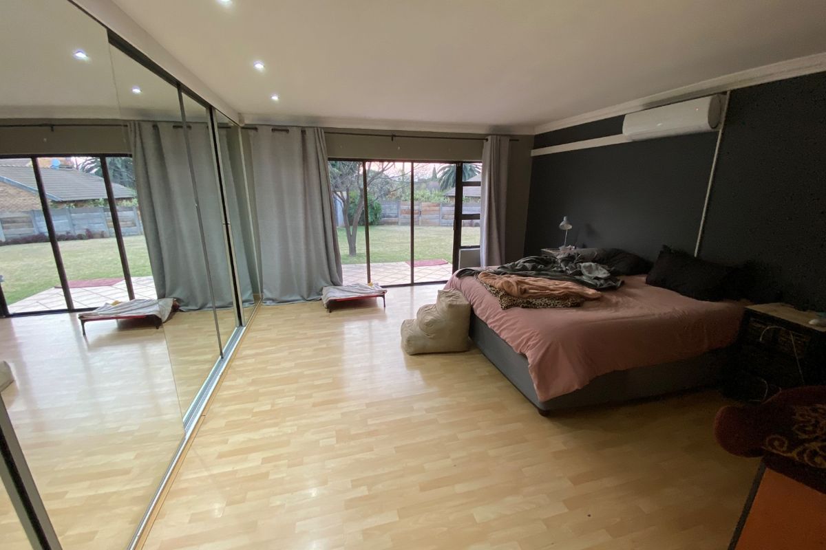 Spacious bedroom featuring laminate flooring, mirrored built-in wardrobes, recessed lighting, and direct access to the rear garden through sliding glass doors.