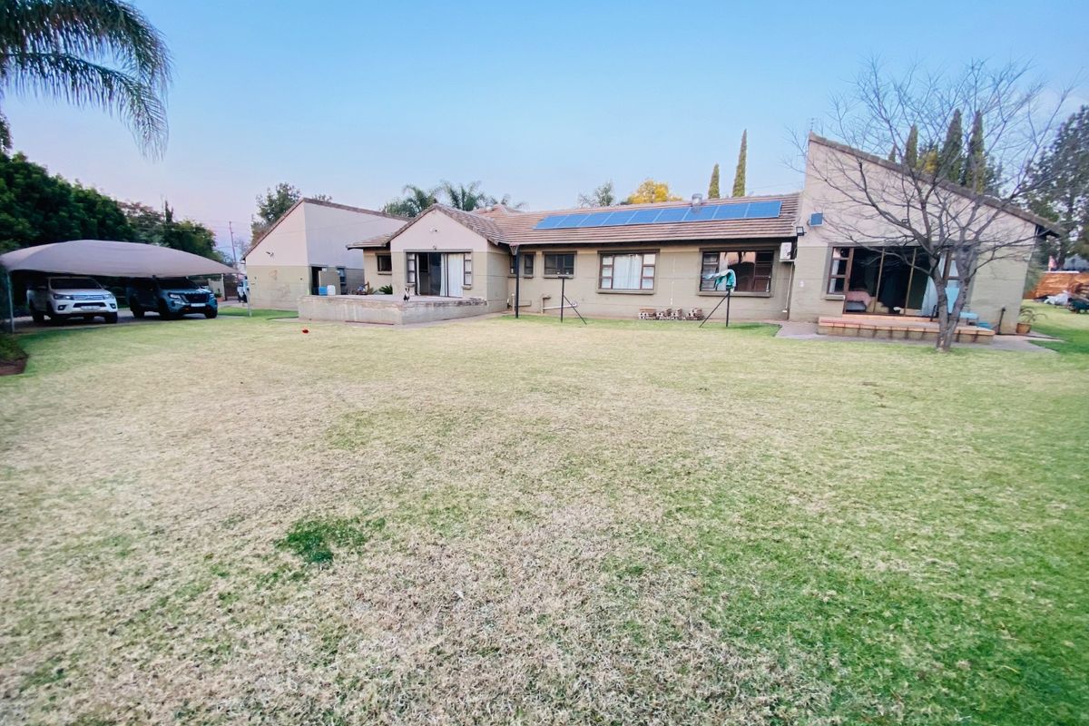 Spacious rear garden view featuring a large lawn, paved patio areas, sliding door access, and roof-mounted solar panels.