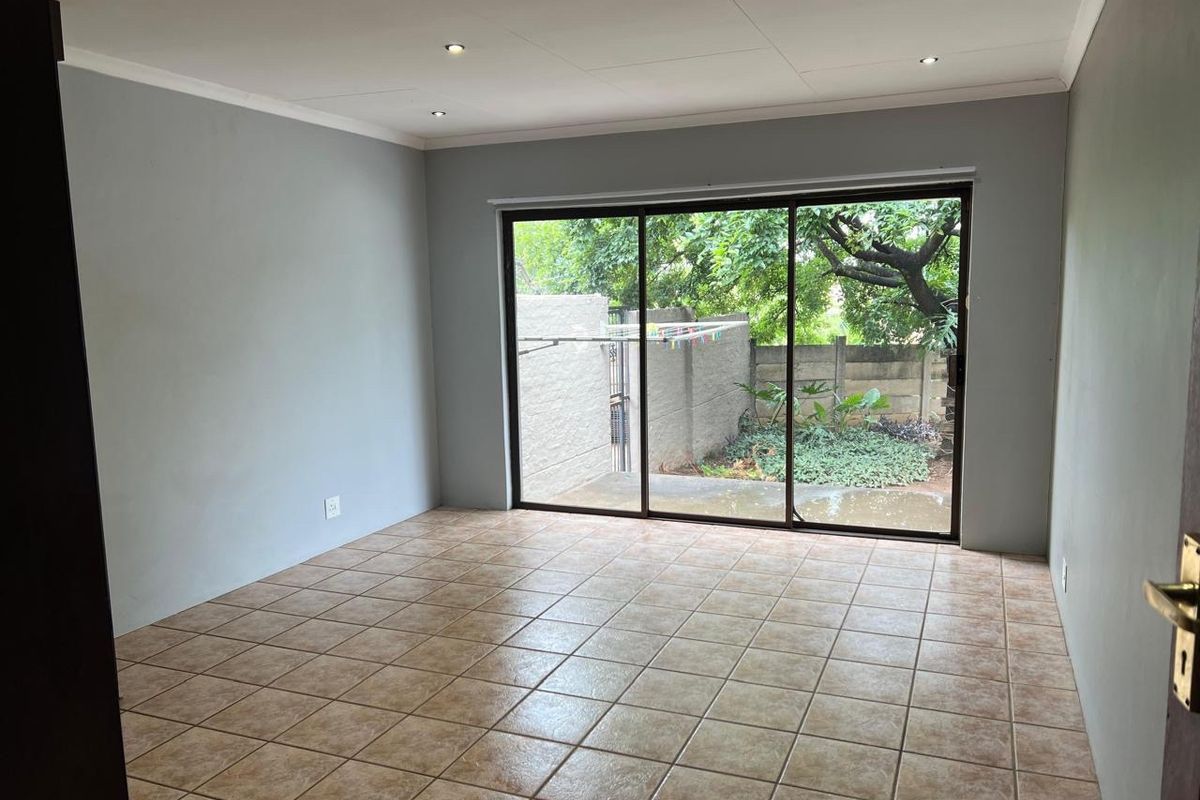 An empty living room featuring neutral grey walls, tiled flooring, and a large sliding glass door providing access to the rear garden area.