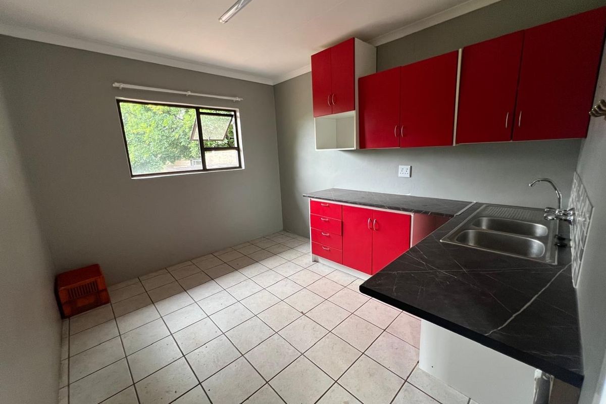 A functional kitchen featuring red cabinetry, dark laminate countertops, a stainless steel double sink, and tiled flooring.