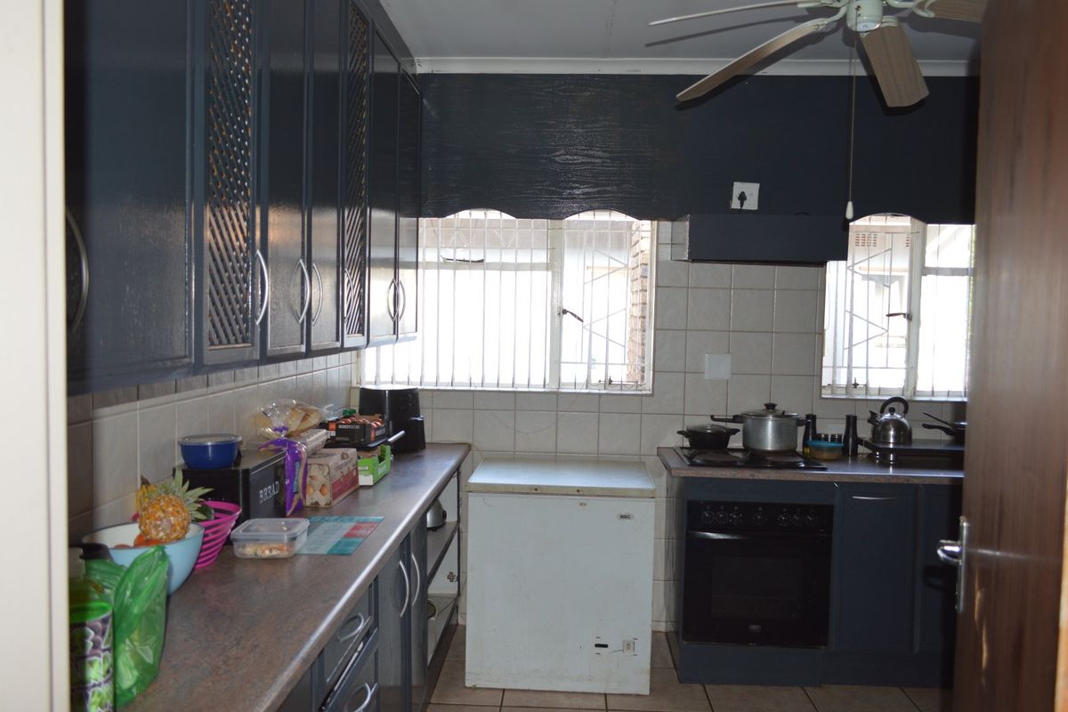 A functional kitchen featuring dark painted cabinetry, tiled backsplash, built-in oven and hob, and security bars on the windows.