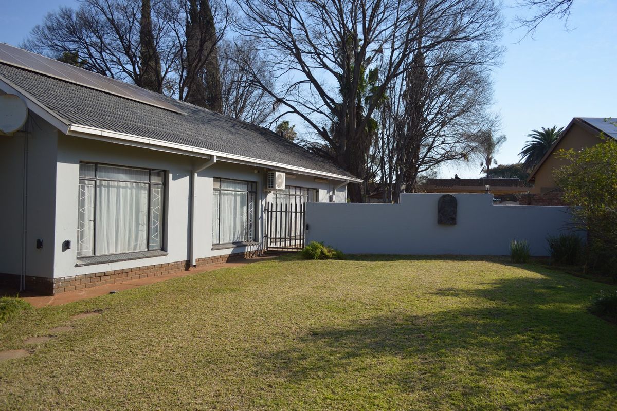 Rear view of the property featuring a well-maintained lawn, perimeter wall, and exterior building facade with solar panels and security features.