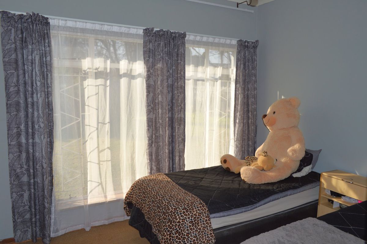 A bedroom featuring large windows with security bars and curtain rails, providing natural light to the space.