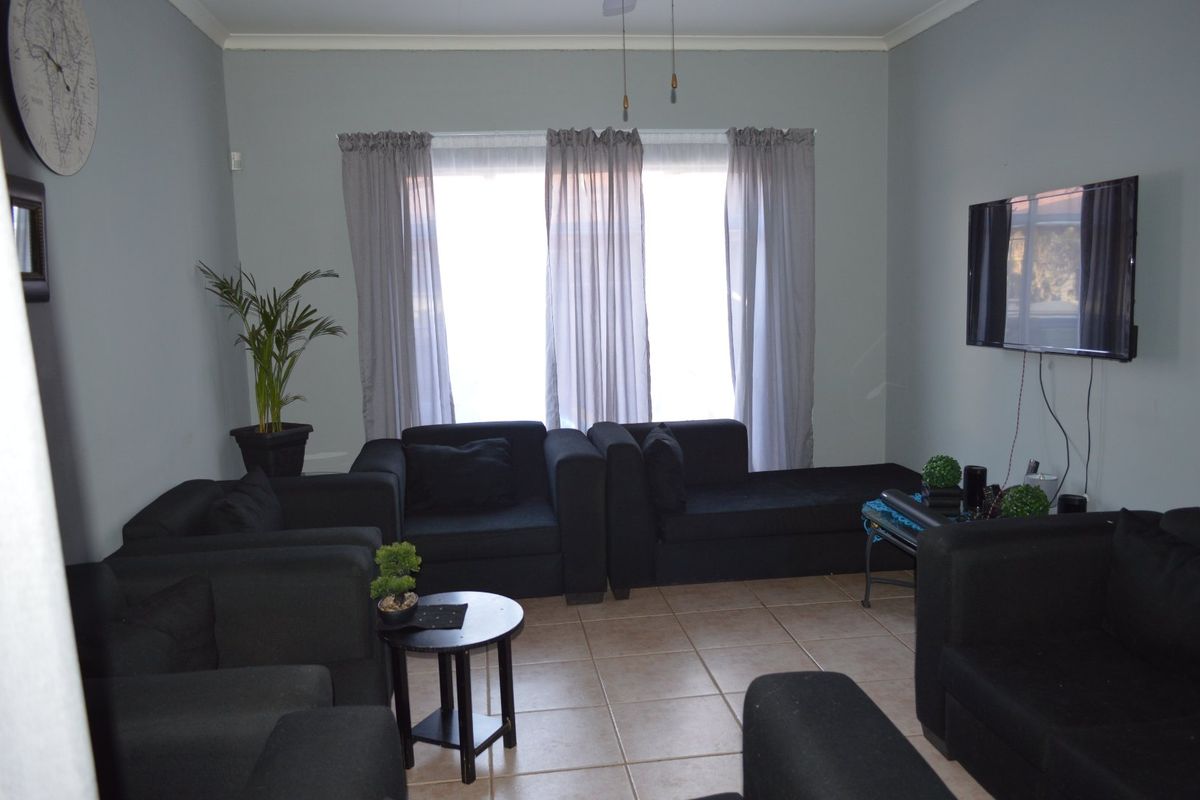 A living room featuring neutral wall tones, tiled flooring, and large windows with curtain treatments, providing a functional and well-lit space.
