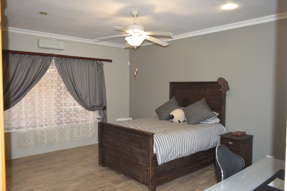 A well-maintained bedroom featuring tiled flooring, a ceiling fan, and a wall-mounted split-system air conditioning unit.