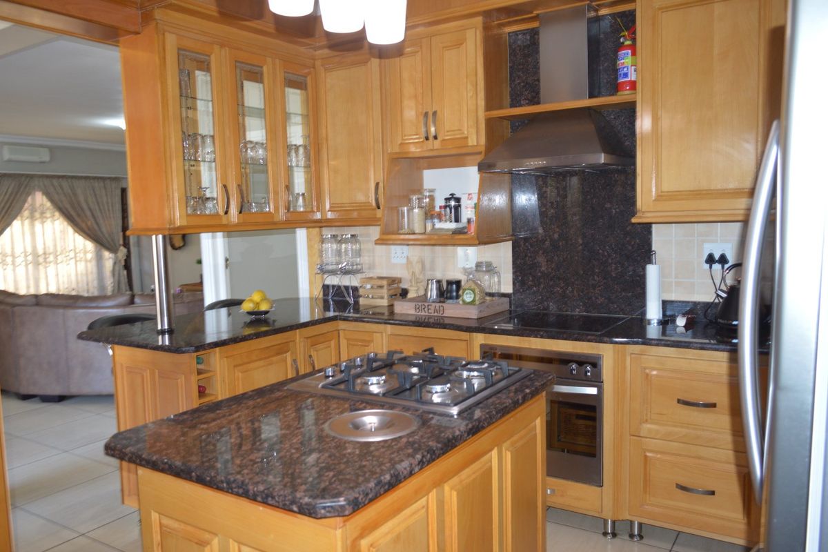A well-maintained kitchen featuring warm wooden cabinetry, granite countertops, a central island with a gas hob, and integrated stainless steel appliances.
