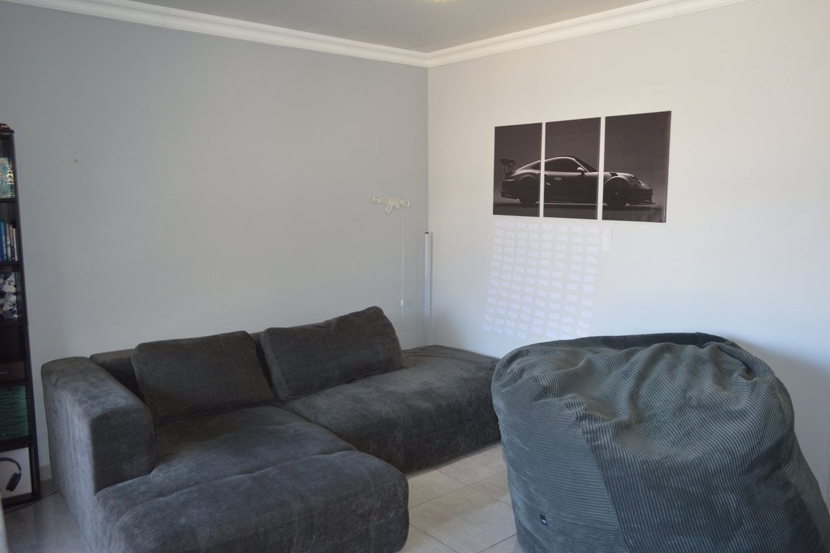 A living room space featuring neutral wall tones, tiled flooring, and crown molding, providing a blank canvas for interior design updates.