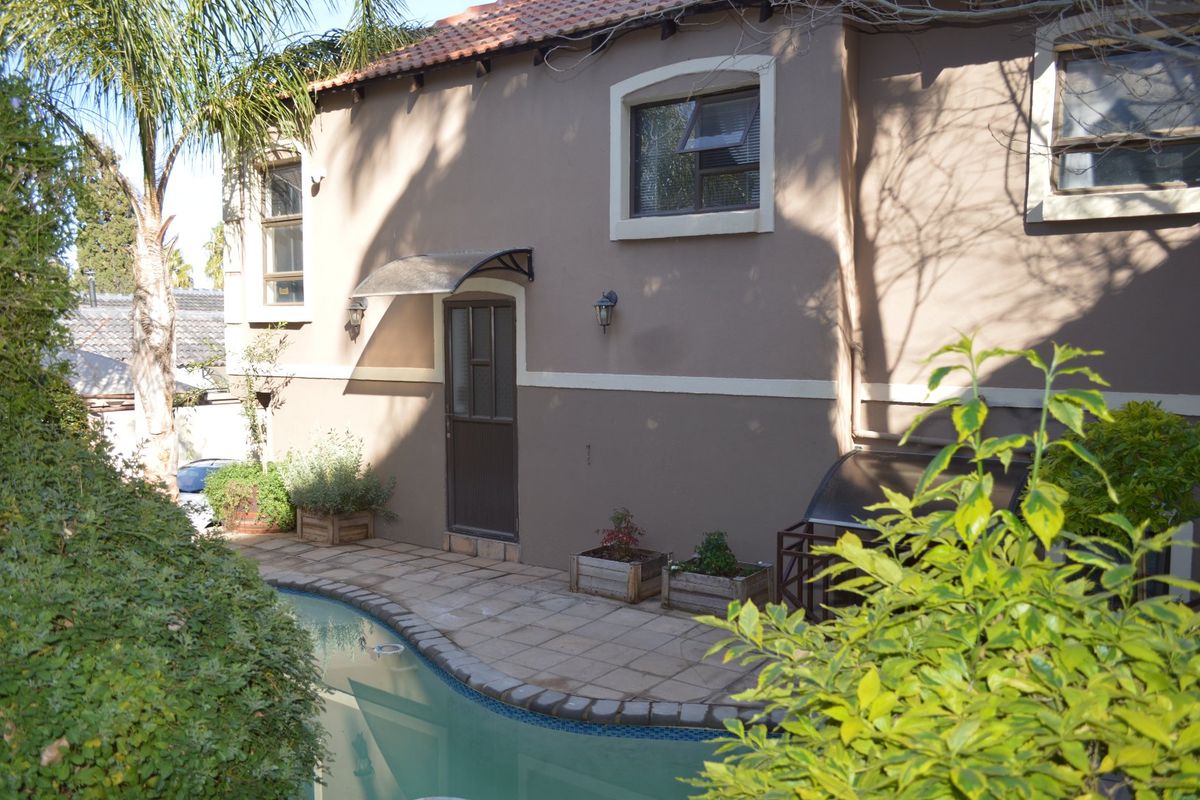 Rear exterior view of the house featuring a paved patio area adjacent to a swimming pool, with exterior wall lighting and an awning.