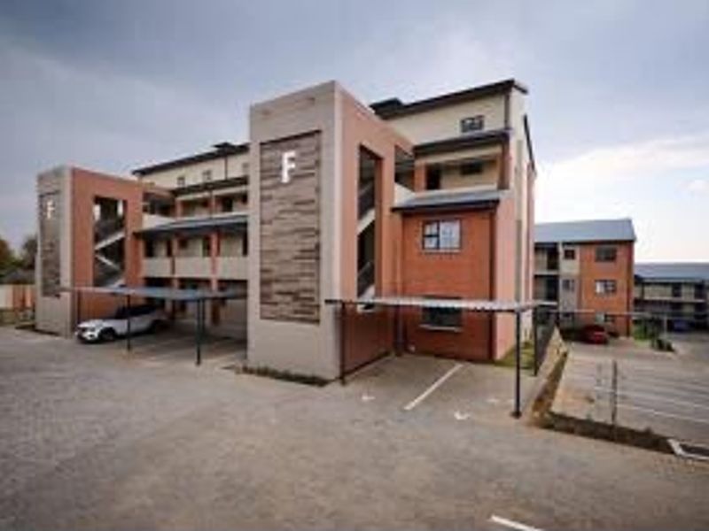 Exterior view of a modern multi-story apartment complex featuring brick facades, covered parking bays, and paved driveway access.