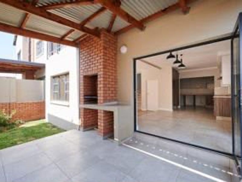 Covered patio featuring a built-in brick braai, timber pergola roof, and large stacking doors providing seamless access to the interior living space.