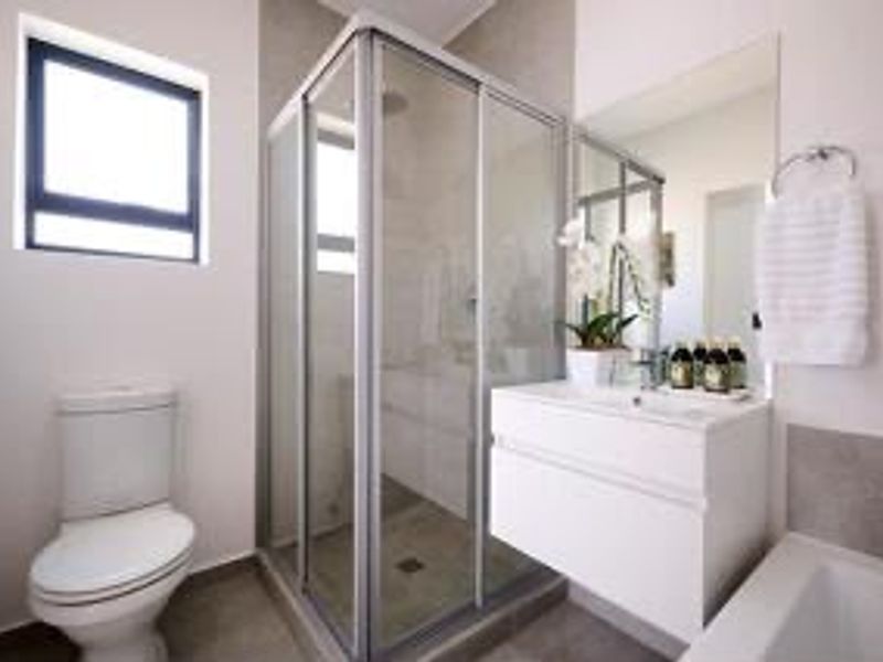 Modern bathroom featuring a glass shower enclosure, wall-mounted vanity, toilet, and bathtub with neutral tiling and clean finishes.