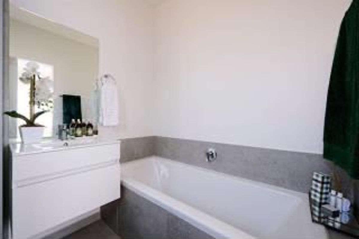 Modern bathroom featuring a wall-mounted vanity with integrated basin, large mirror, and a built-in bathtub with neutral tiled surround.