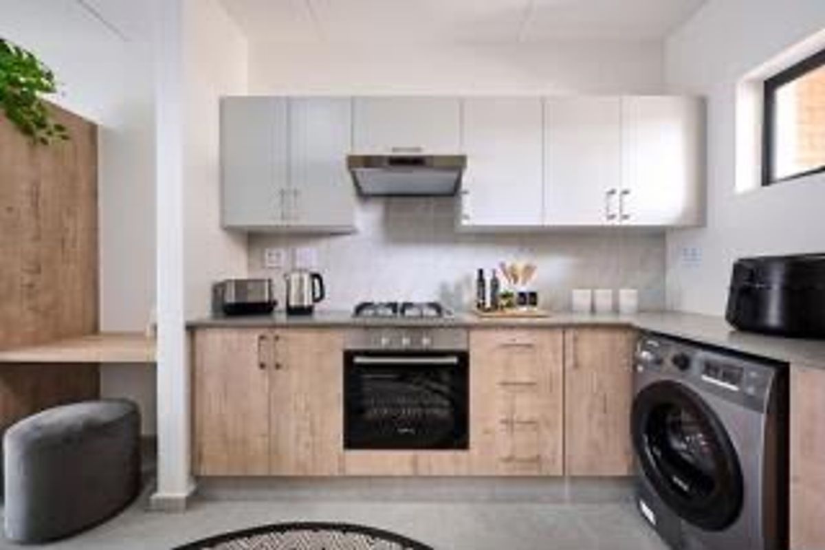 Modern kitchen featuring light wood-look cabinetry, stone countertops, built-in oven and hob, extractor fan, and integrated space for laundry appliances.