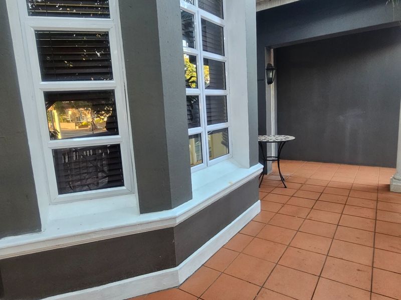 A covered patio area featuring terracotta-style floor tiles, a white timber balustrade, and a bay window overlooking the outdoor space.