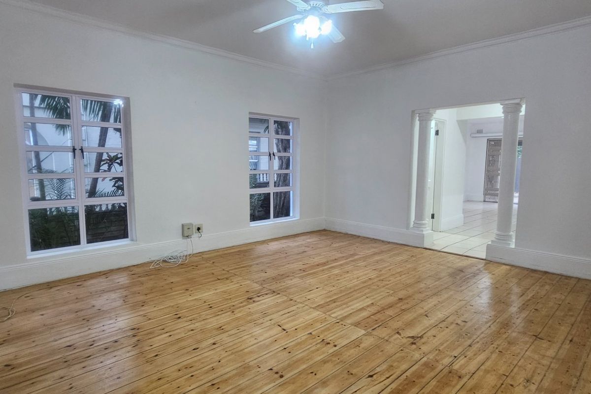 A bright, empty living room featuring polished timber flooring, a ceiling fan, and decorative columns leading to an adjacent space.