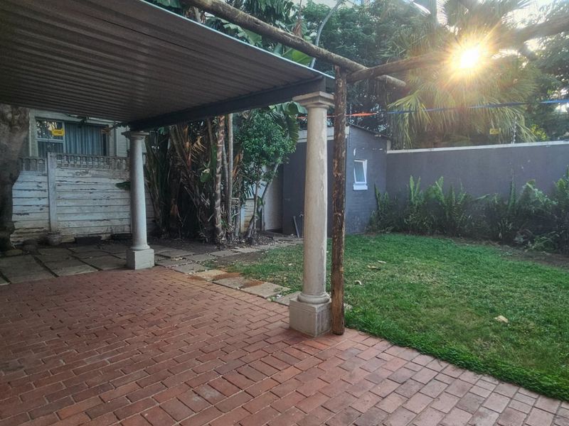 A covered brick-paved patio area overlooking a private garden, featuring structural columns and perimeter boundary walls with integrated electric fencing.