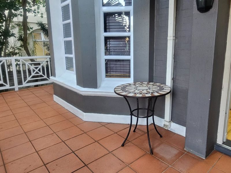 A covered balcony area featuring tiled flooring, a white balustrade, and access to an external staircase.