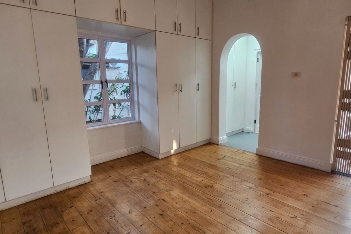 A bright bedroom featuring polished timber flooring, extensive built-in cabinetry, and an arched doorway leading to an adjoining space.