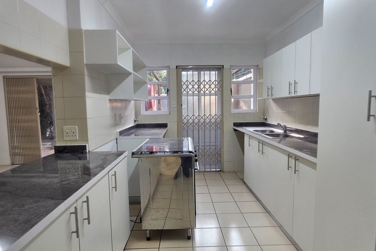 A functional kitchen featuring white cabinetry, dark laminate countertops, tiled flooring, and a stainless steel stove, with direct access to an outdoor area.