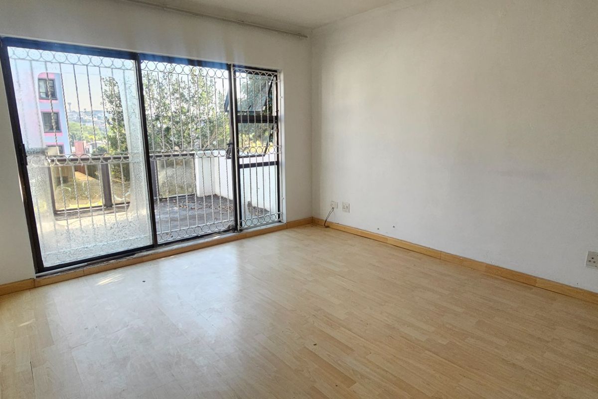 An empty bedroom featuring laminate flooring and a sliding glass door with security bars, providing access to an outdoor balcony area.