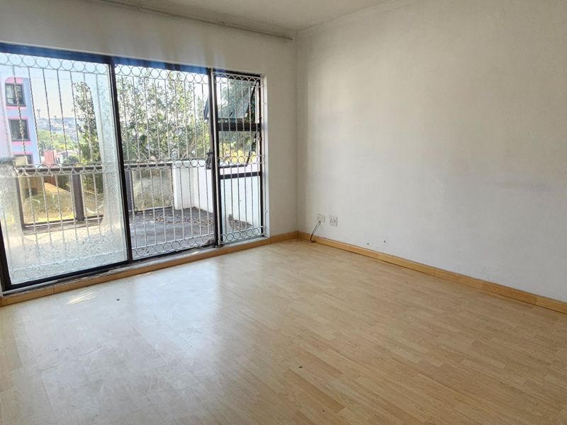 An empty bedroom featuring laminate flooring and a sliding glass door with security bars, providing access to an outdoor balcony area.