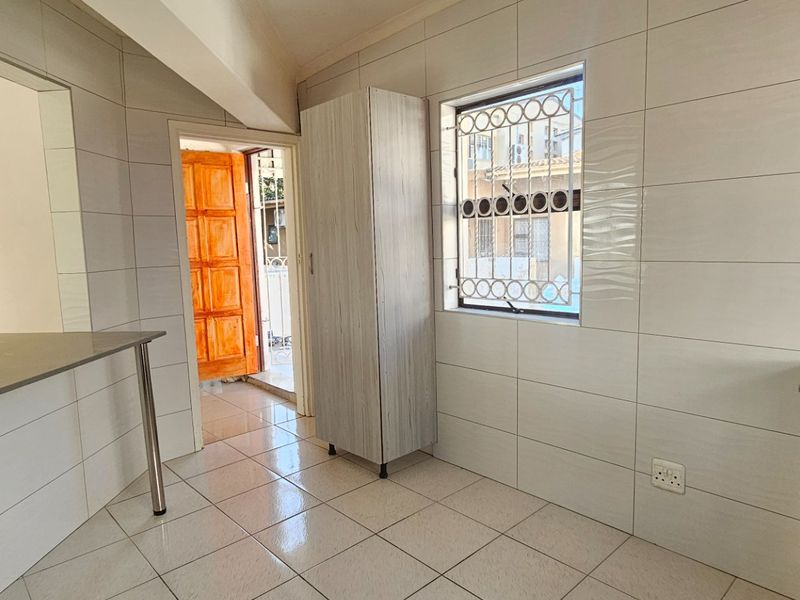 A functional kitchen area featuring tiled walls and flooring, a built-in oven and hob, and a breakfast counter, with direct access to the exterior.