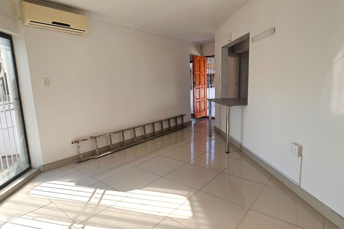 An open-plan living area featuring tiled flooring, a wall-mounted air conditioning unit, and a breakfast bar counter connecting to the kitchen area.