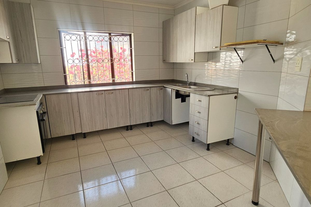 A functional kitchen featuring tiled surfaces, built-in cabinetry, and a window with security bars. The space is currently vacant and ready for updates.
