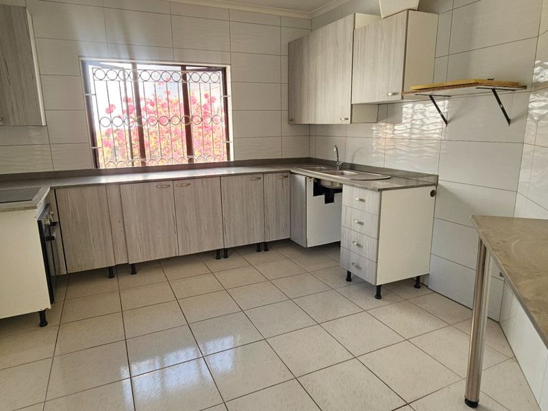 A functional kitchen featuring tiled surfaces, built-in cabinetry, and a window with security bars. The space is currently vacant and ready for updates.