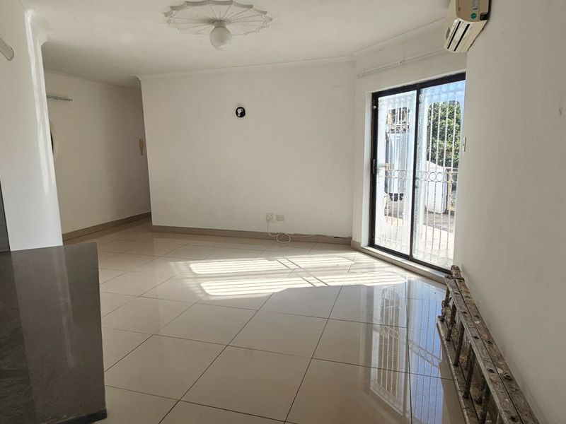 An open-plan living and kitchen area featuring neutral tiled flooring, a sliding door to the exterior, and a wall-mounted air conditioning unit.