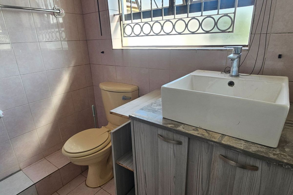 A compact bathroom featuring a vessel sink on a vanity cabinet, a toilet, and tiled finishes, requiring cosmetic updates to modernize the space.