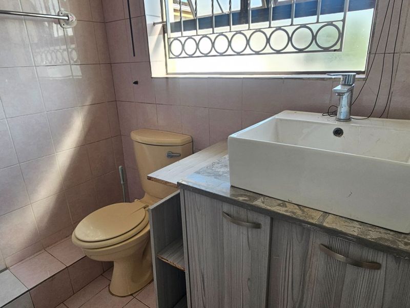 A compact bathroom featuring a vessel sink on a vanity cabinet, a toilet, and tiled finishes, requiring cosmetic updates to modernize the space.