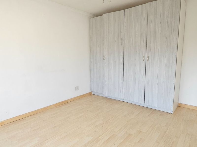 A bright, empty bedroom featuring light-toned laminate flooring and a large, modern built-in wardrobe with wood-grain finish.