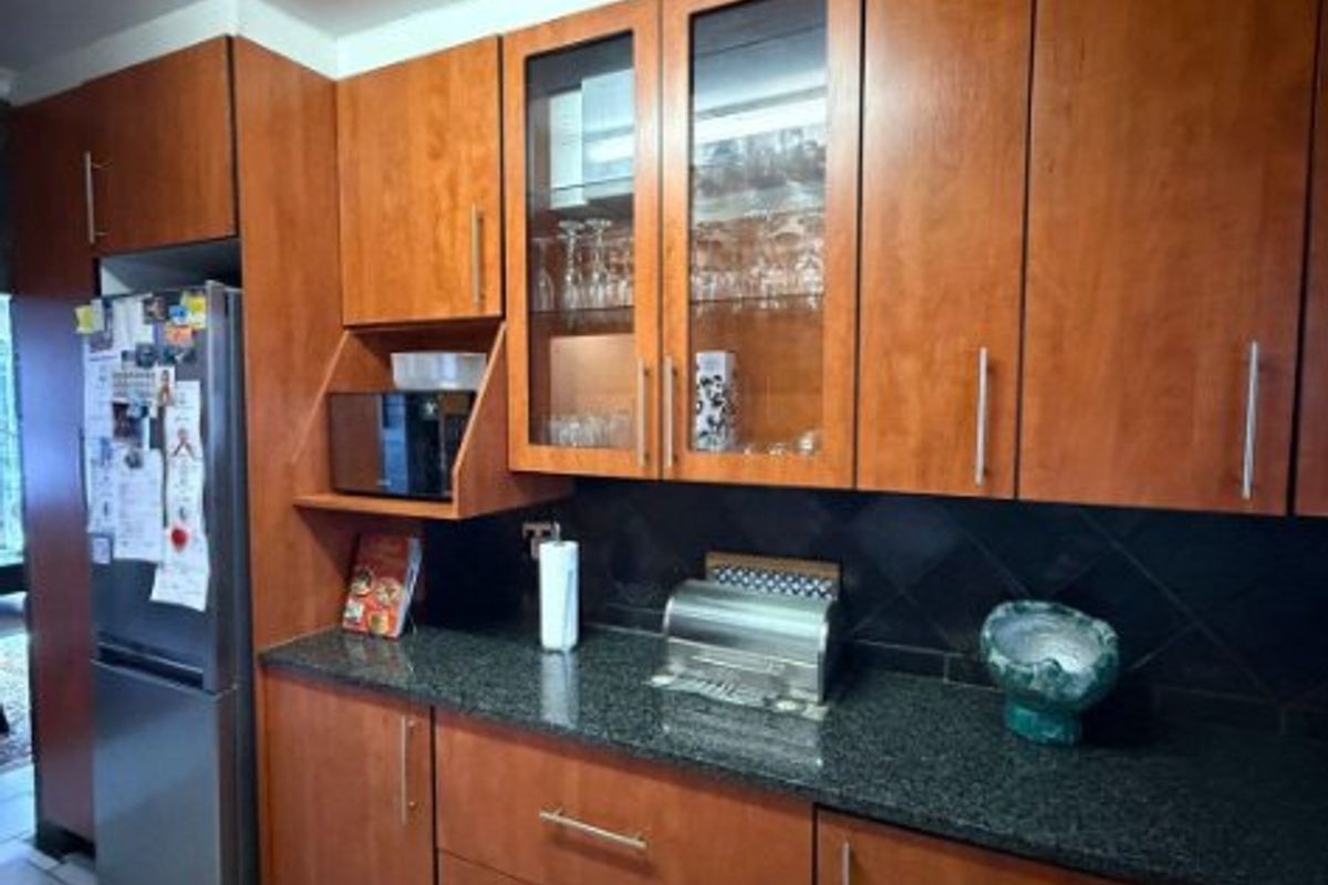 A functional kitchen featuring warm-toned wooden cabinetry, dark granite countertops, a tiled backsplash, and glass-front display cabinets for storage.