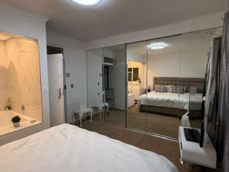 Spacious bedroom featuring a built-in mirrored wardrobe and an integrated en-suite bathtub area, offering a functional layout with carpeted flooring.