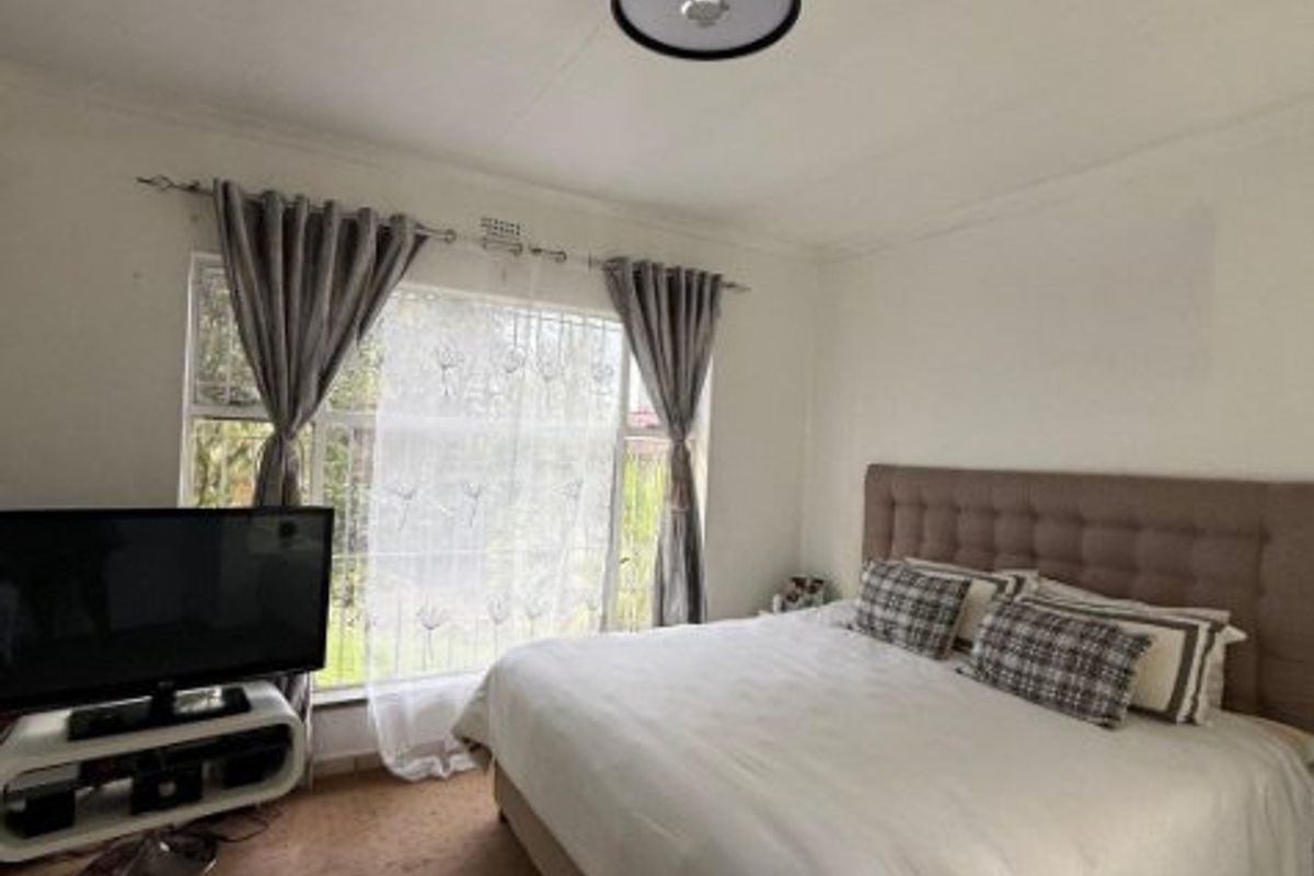 A standard bedroom featuring a large window with security bars, neutral wall finishes, and carpeted flooring.