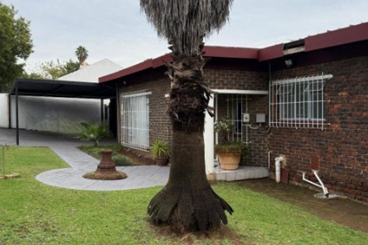 Rear exterior view of the house featuring a brick facade, security bars on windows, a paved walkway, and a carport area.