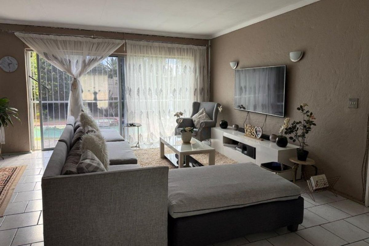 A comfortable living room featuring tiled flooring, wall-mounted lighting, and a large sliding glass door providing access to the outdoor area.