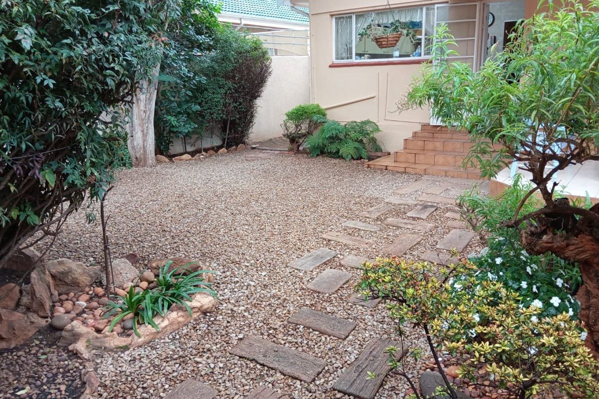 A low-maintenance rear garden area featuring gravel landscaping, stone paver pathways, and tiled entrance steps leading to the home.