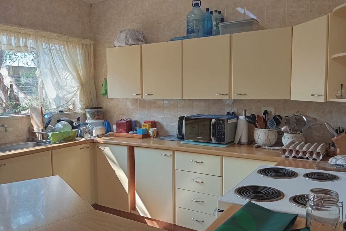 A functional kitchen featuring laminate countertops, built-in cabinetry, a tiled backsplash, and an electric hob, offering a practical layout for daily meal preparation.