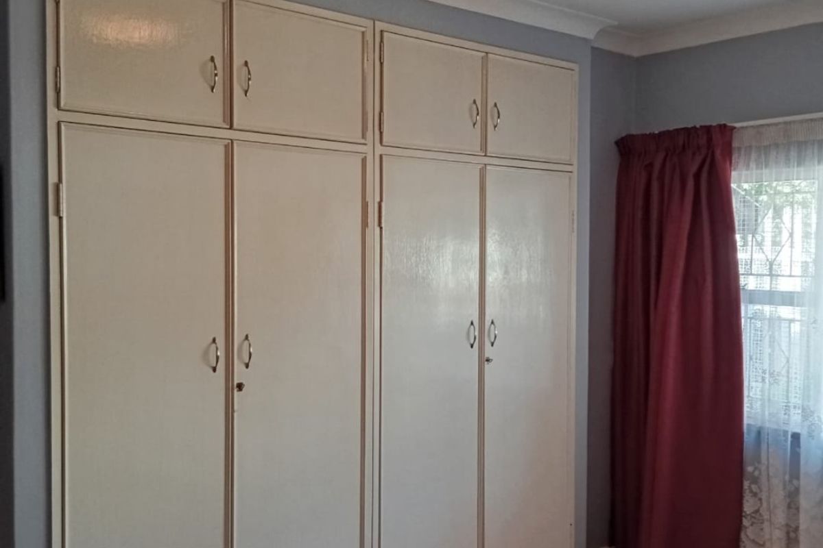 A bedroom featuring extensive built-in floor-to-ceiling cupboards, laminate flooring, and neutral wall finishes.