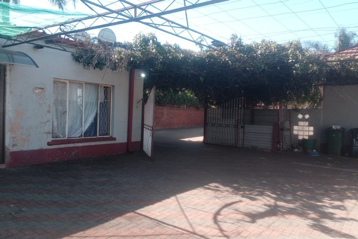 Rear exterior area featuring a paved driveway, metal pergola structure, and secure gated access with perimeter brick walling.